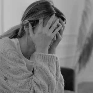Stress. En kvinde tager sig til hovedet og ser besværet ud.
