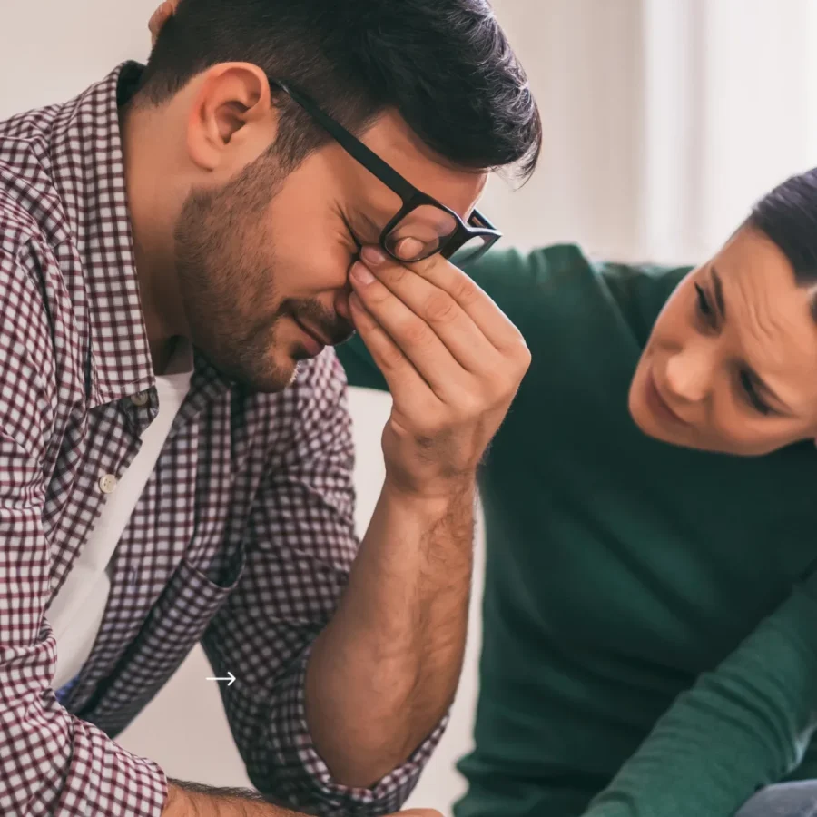 Depression. Mand tager sig til øjnene og ser besværet ud, mens en kvinde trøster ham.